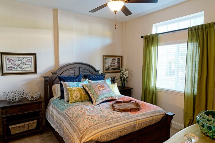 A cozy bedroom with a large bed, colorful pillows, and a ceiling fan.