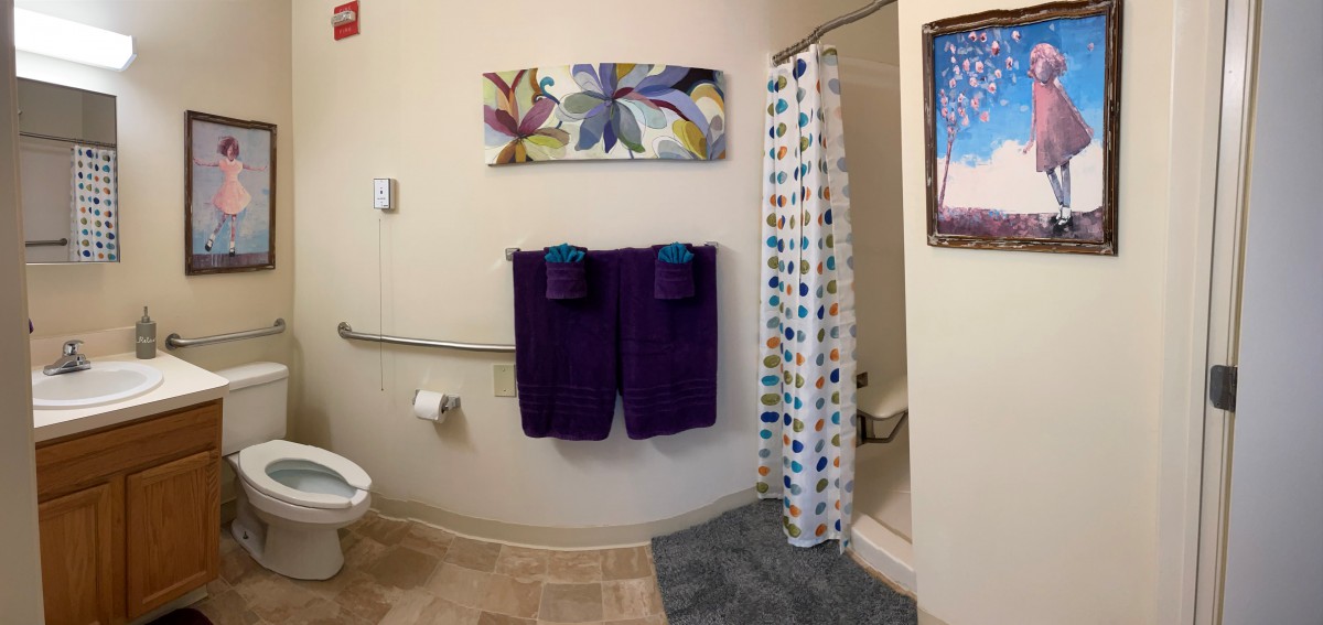 A neatly decorated bathroom featuring purple towels, a colorful shower curtain, and vibrant artwork on the wall.