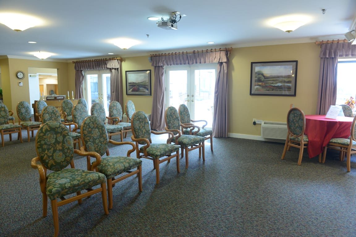 An empty meeting room with arranged chairs, large windows, and paintings on the walls.