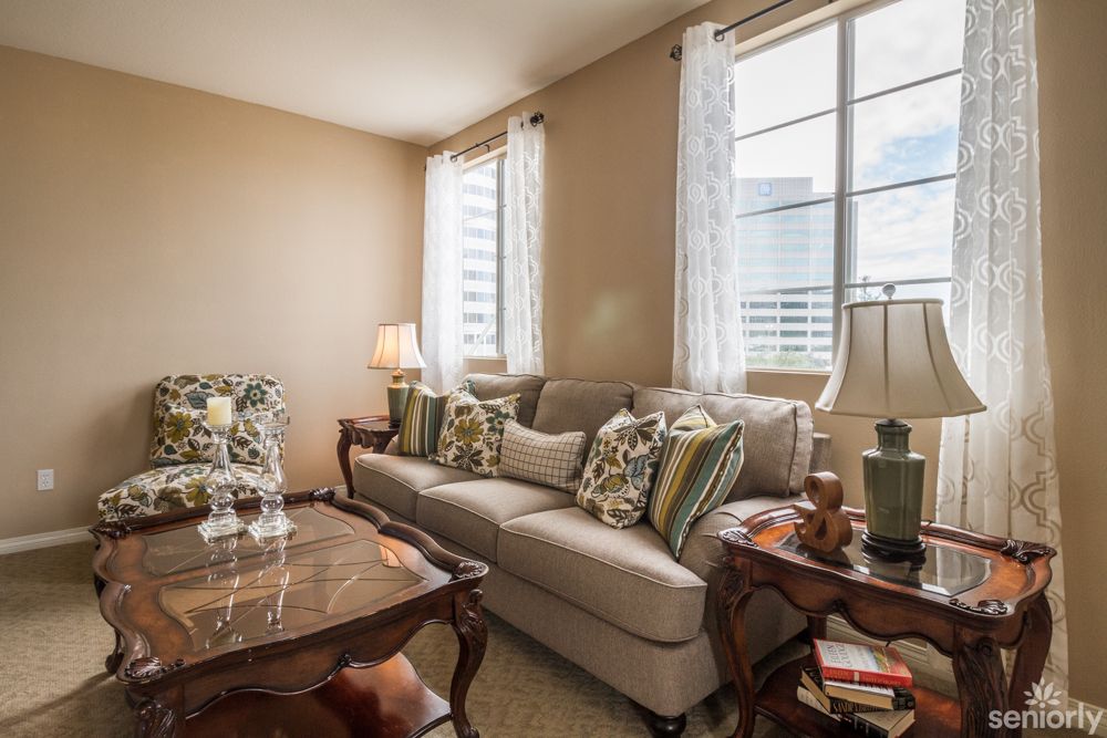 A cozy living room featuring a comfortable sofa with patterned cushions, a wooden coffee table, and large windows adorned with sheer curtains.