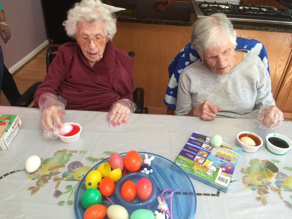 Two elderly women painting colorful Easter eggs together at a table.