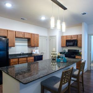 A modern kitchen with a granite countertop, wooden cabinets, and pendant lighting.