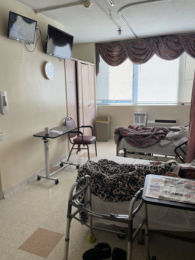 A hospital room with a patient bed, medical equipment, and a chair next to a window with curtains.