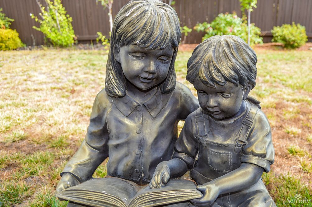 A statue of two children reading a book together in an outdoor setting.