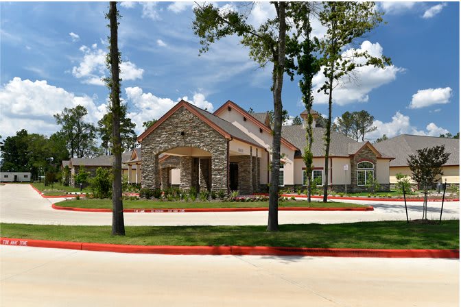 A large, modern house with stone exterior and a well-maintained driveway surrounded by trees under a clear sky.