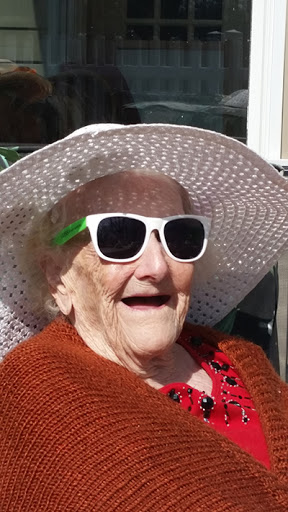 An elderly woman enjoying the sunny weather, wearing stylish sunglasses and a wide-brimmed sunhat.