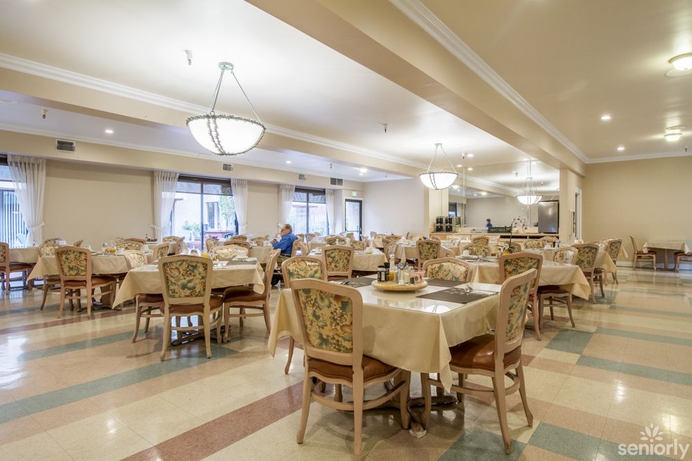 An elegant and spacious dining room with neatly arranged tables and chairs, illuminated by chandeliers.