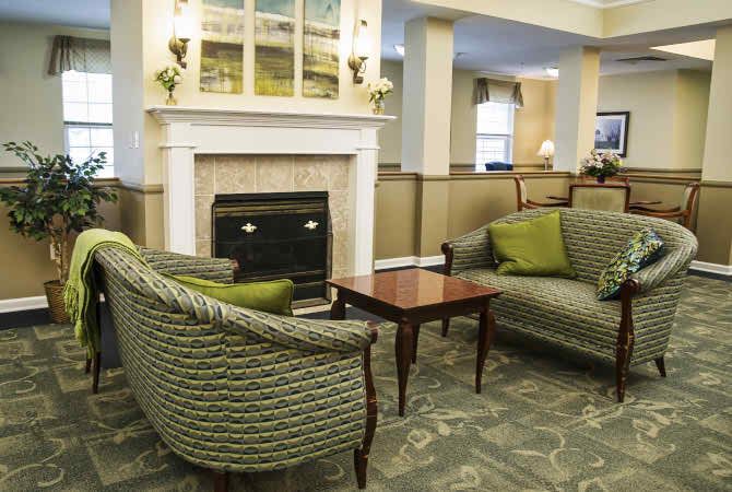 A cozy living room with a fireplace, featuring green sofas and a wooden coffee table.