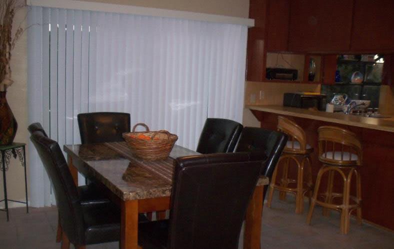 A dining area featuring a table with chairs and a basket centerpiece, adjacent to a kitchen.