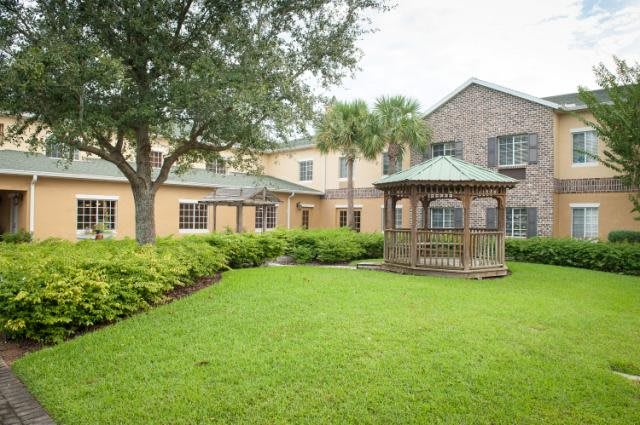 A charming house with a well-maintained yard and a wooden gazebo surrounded by trees.