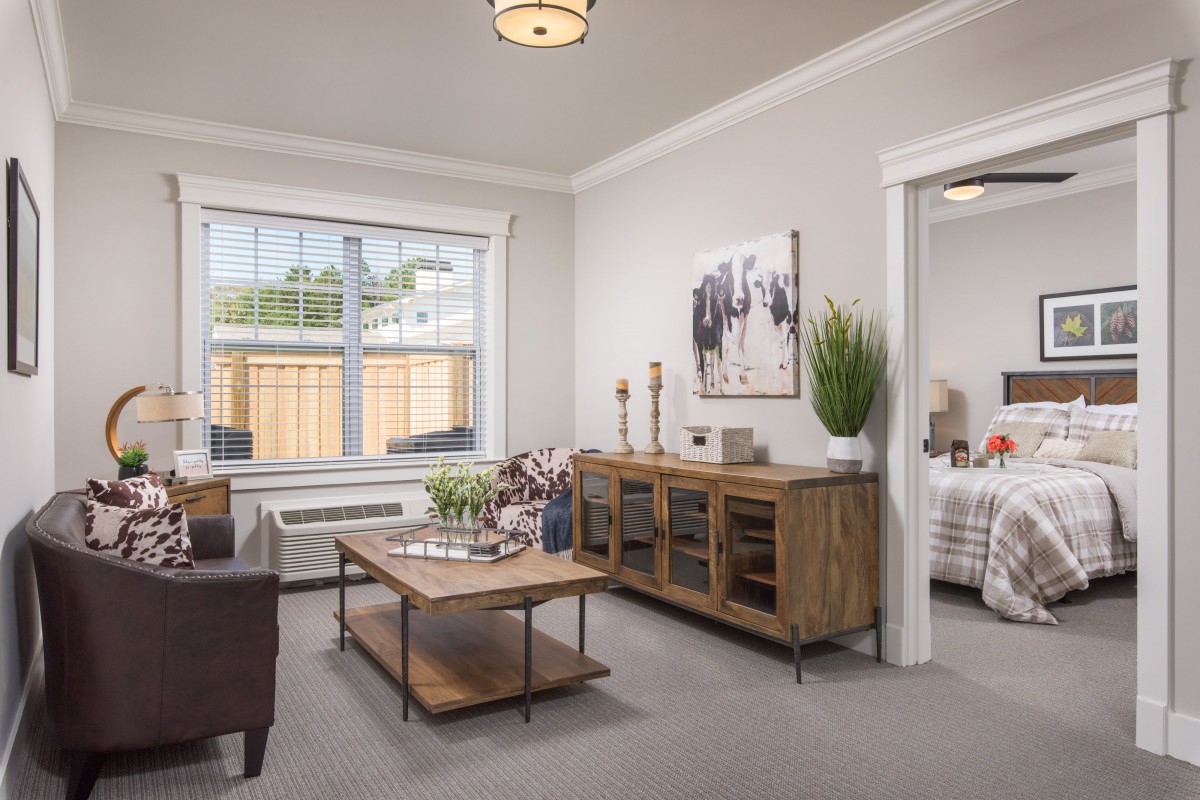 A modern living room with neutral tones, featuring wooden furniture and ample natural light.
