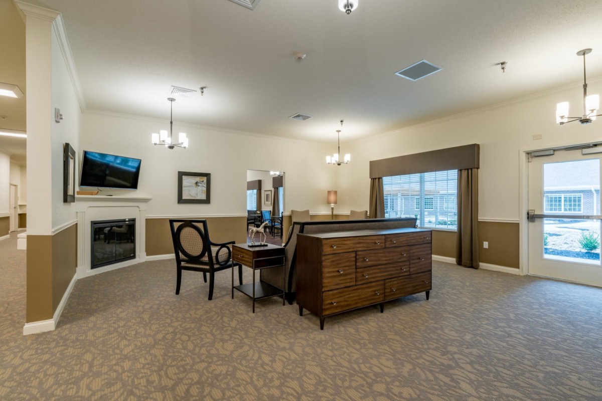 A spacious living room featuring a fireplace, a television mounted on the wall, and various pieces of furniture including a desk and chairs.