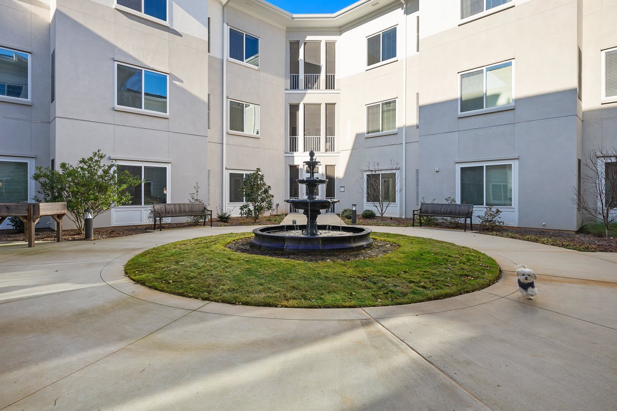 A peaceful courtyard featuring a central fountain with surrounding benches and a modern building exterior.