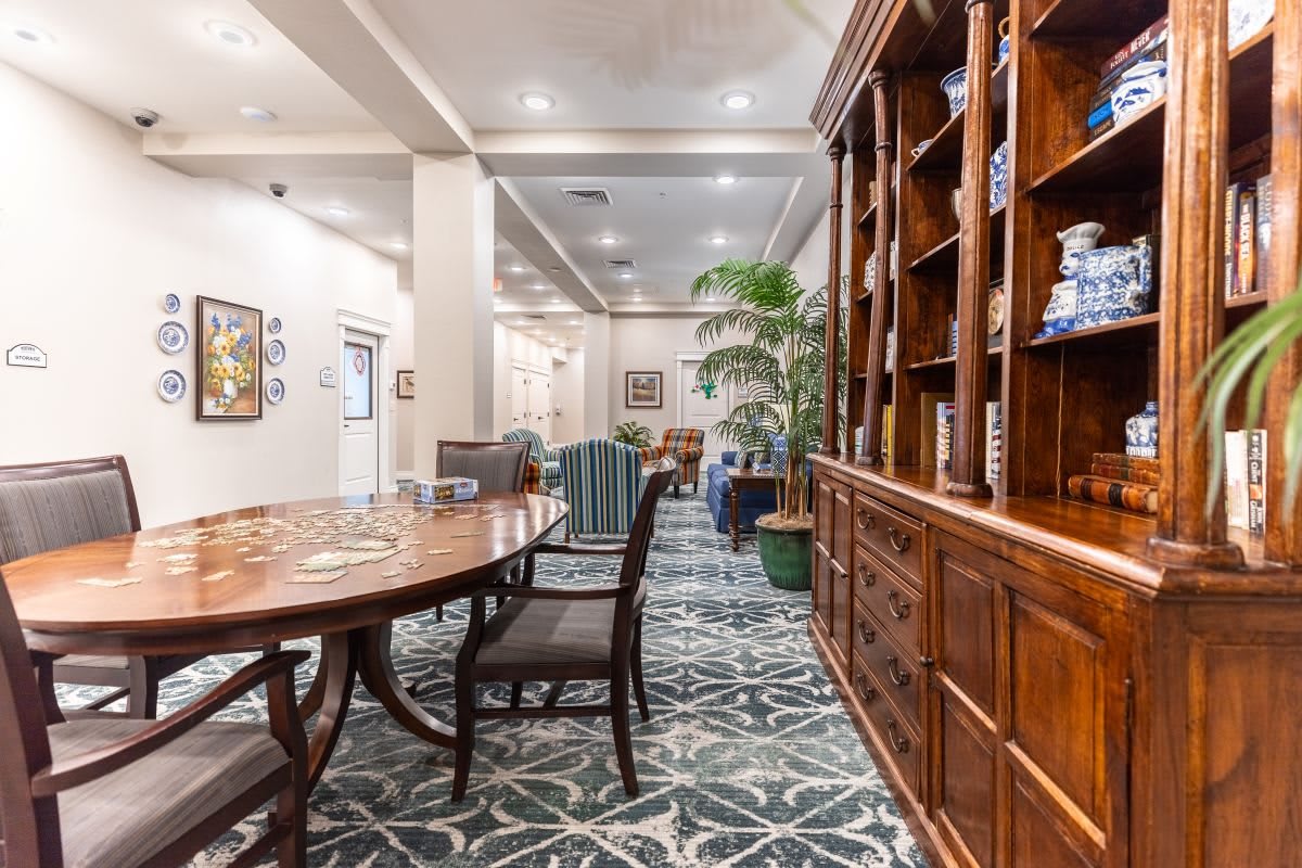 A cozy library interior with a wooden table, chairs, and an extensive bookshelf.
