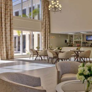 A modern and elegant lobby with a seating area, large windows, and a chandelier.