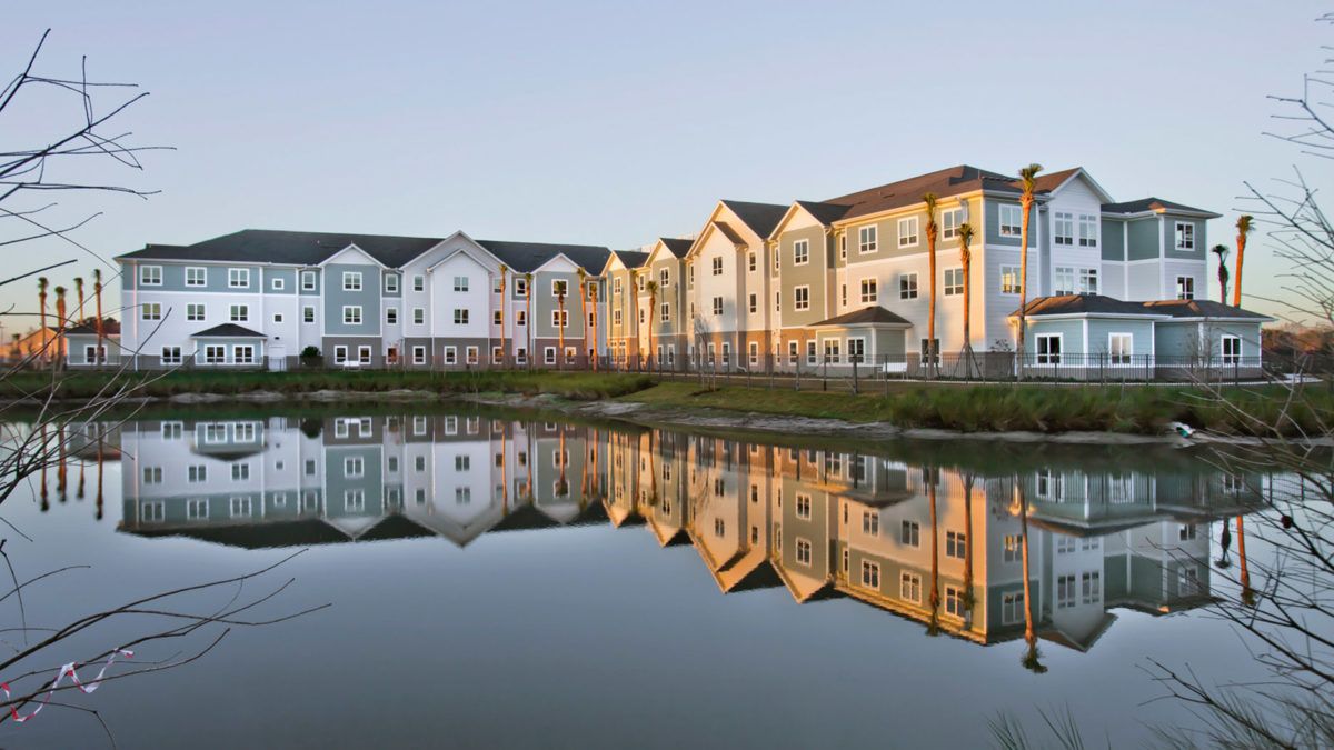 A row of modern apartments reflecting on a calm lake during sunset.