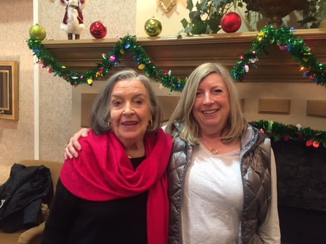 Two women smiling in front of a festive, decorated fireplace.