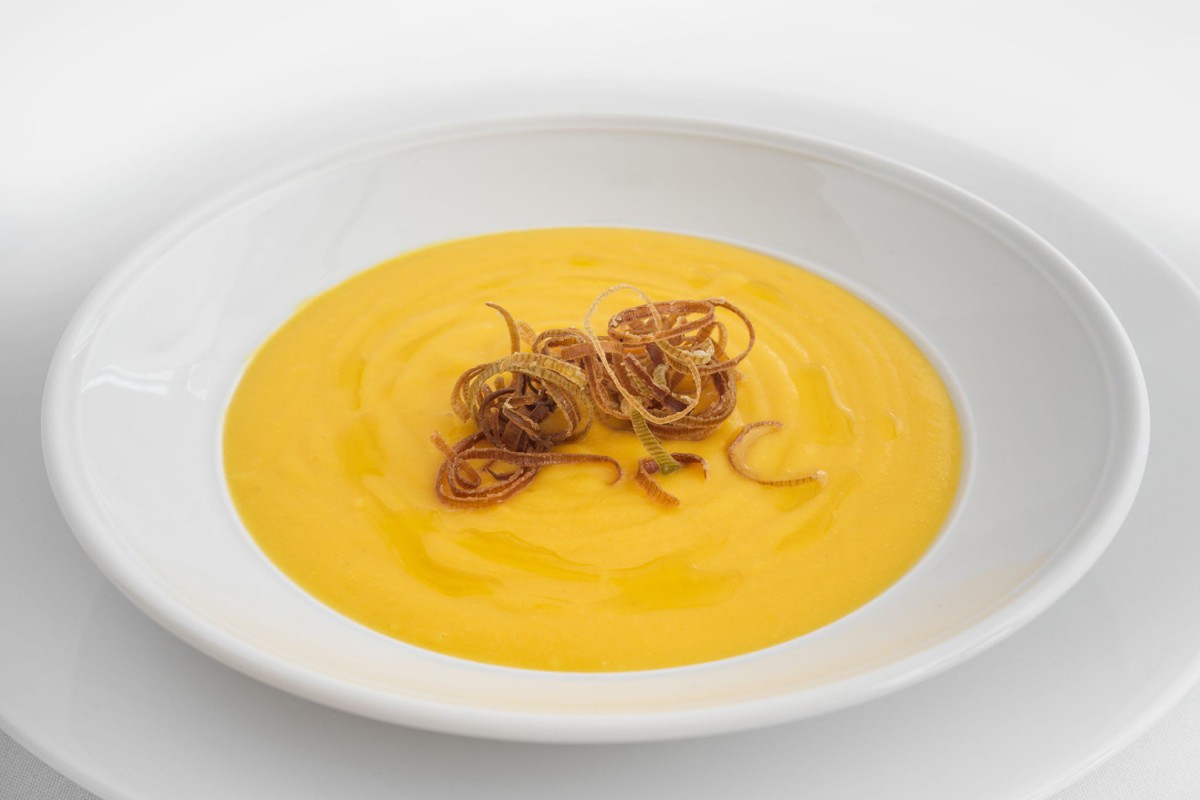 A bowl of creamy pumpkin soup garnished with crispy onion straws.