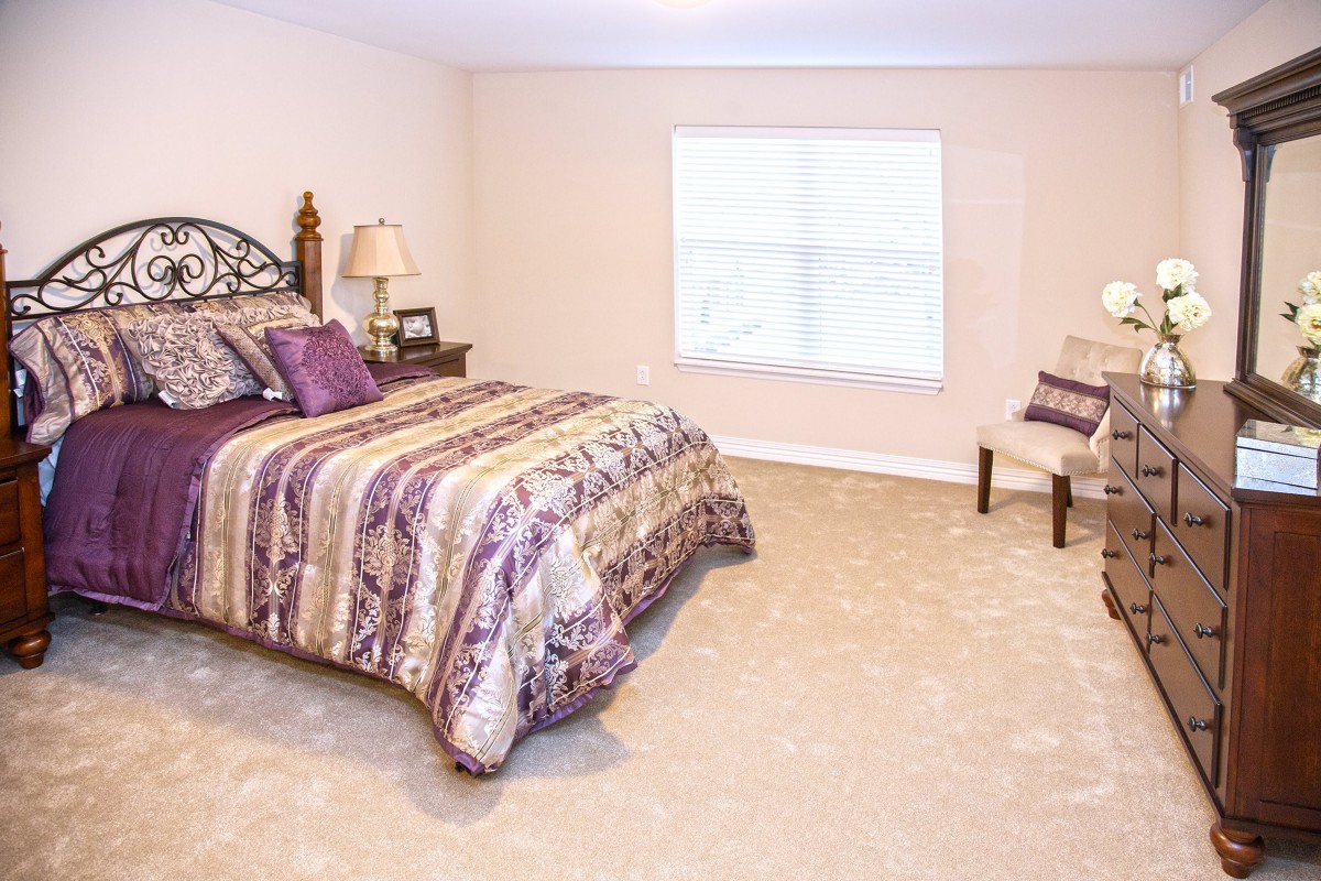 A cozy bedroom with a patterned bedspread, carpet flooring, and a window.
