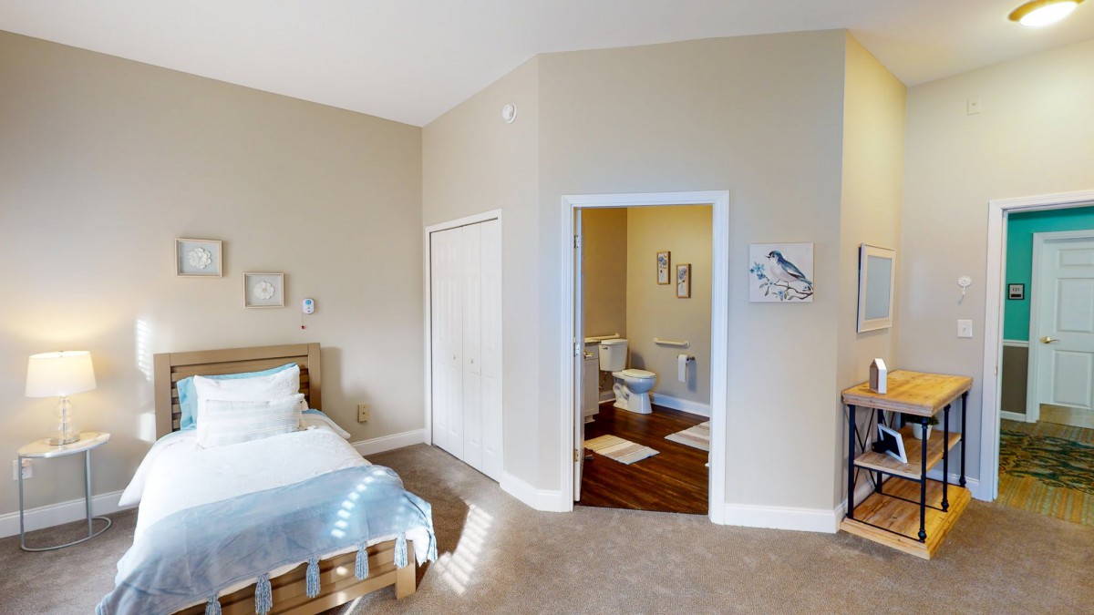 A cozy bedroom with a view into an adjoining bathroom, featuring neutral tones and simple decor.