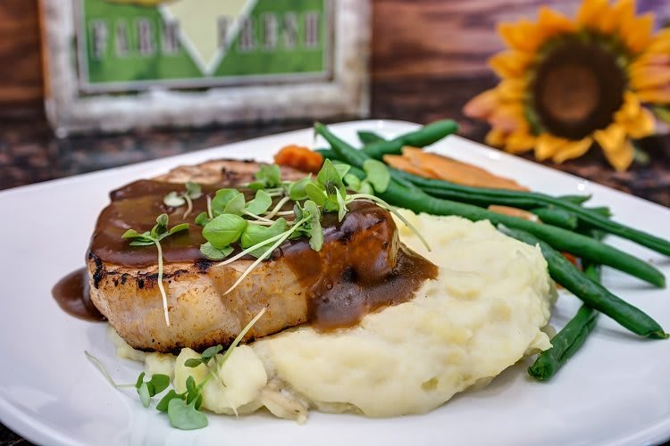 A gourmet pork chop served with mashed potatoes and green beans, elegantly garnished and plated.