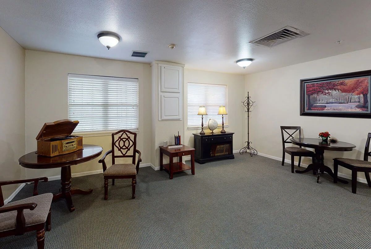 A cozy room interior with chairs, a table, lamps, and windows.
