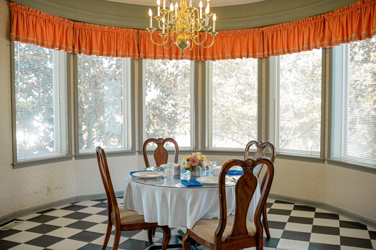 Elegant dining room with a round table set for breakfast, featuring large windows and a classic chandelier.