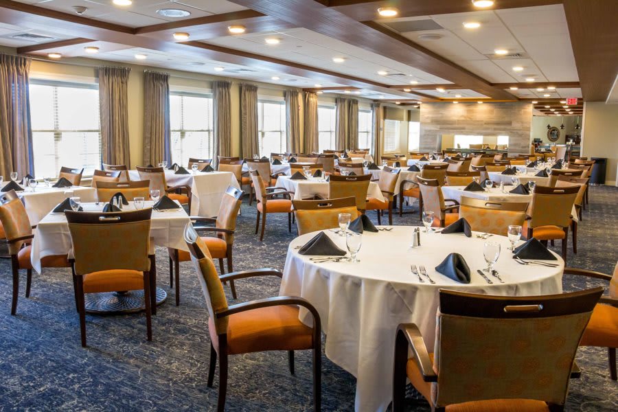 An elegantly set dining room with round tables and chairs arranged for an event or meal.