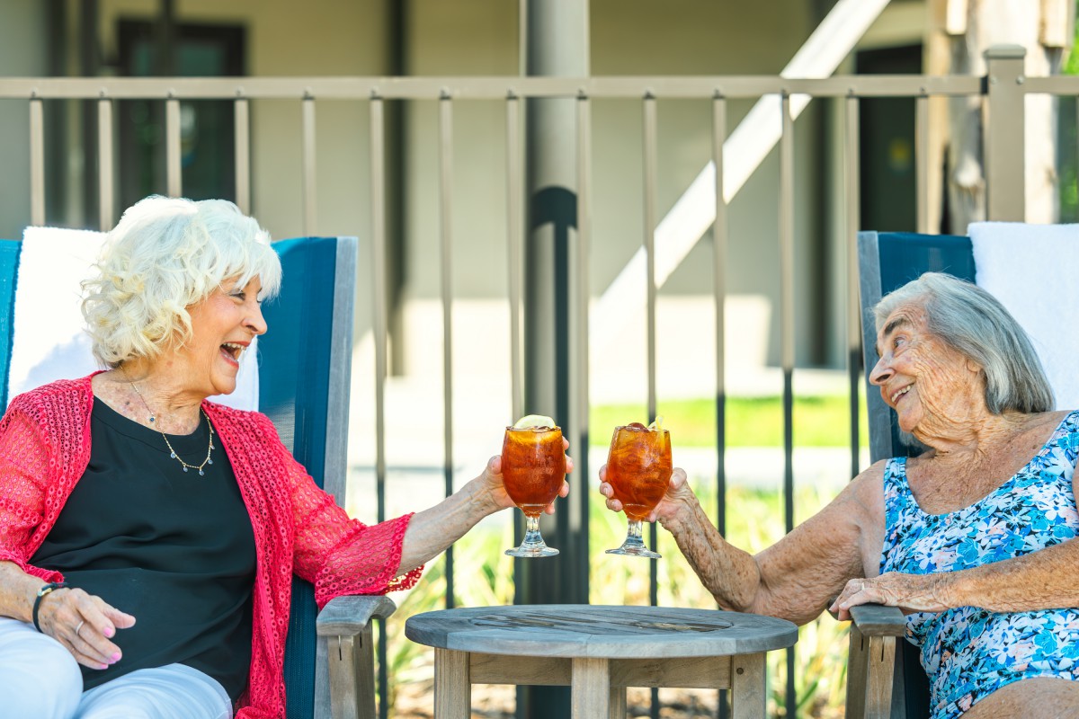Two elderly friends enjoying drinks and conversing outdoors.