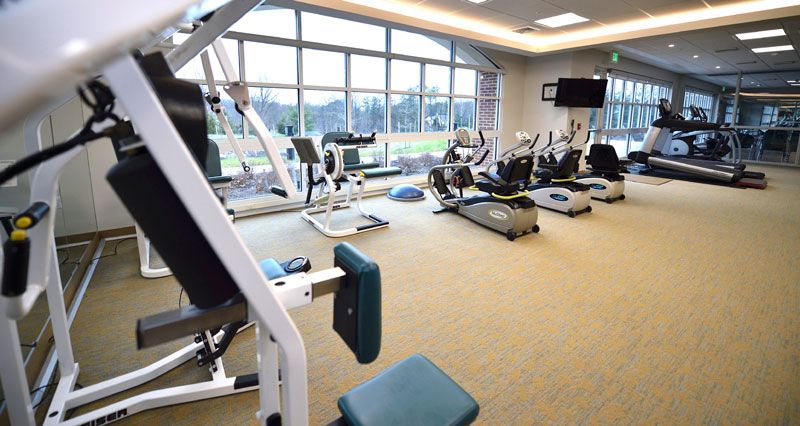 A well-equipped gym featuring various fitness machines and a large window with natural light.