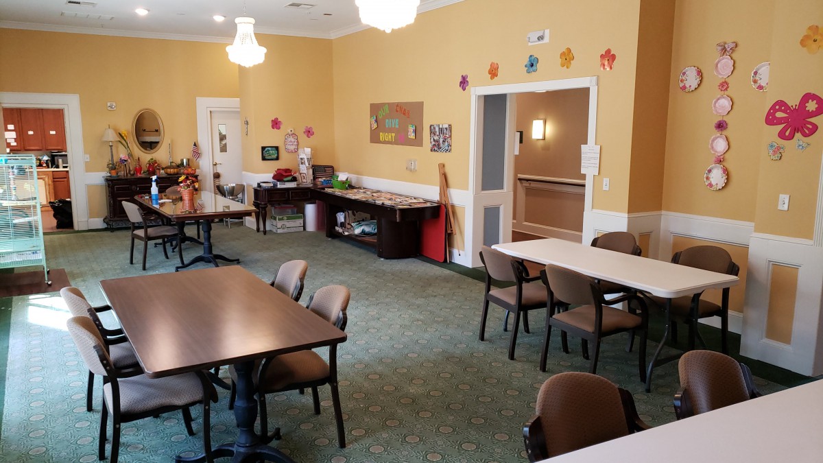 A well-lit community room with tables, chairs, and art supplies arranged for activities.