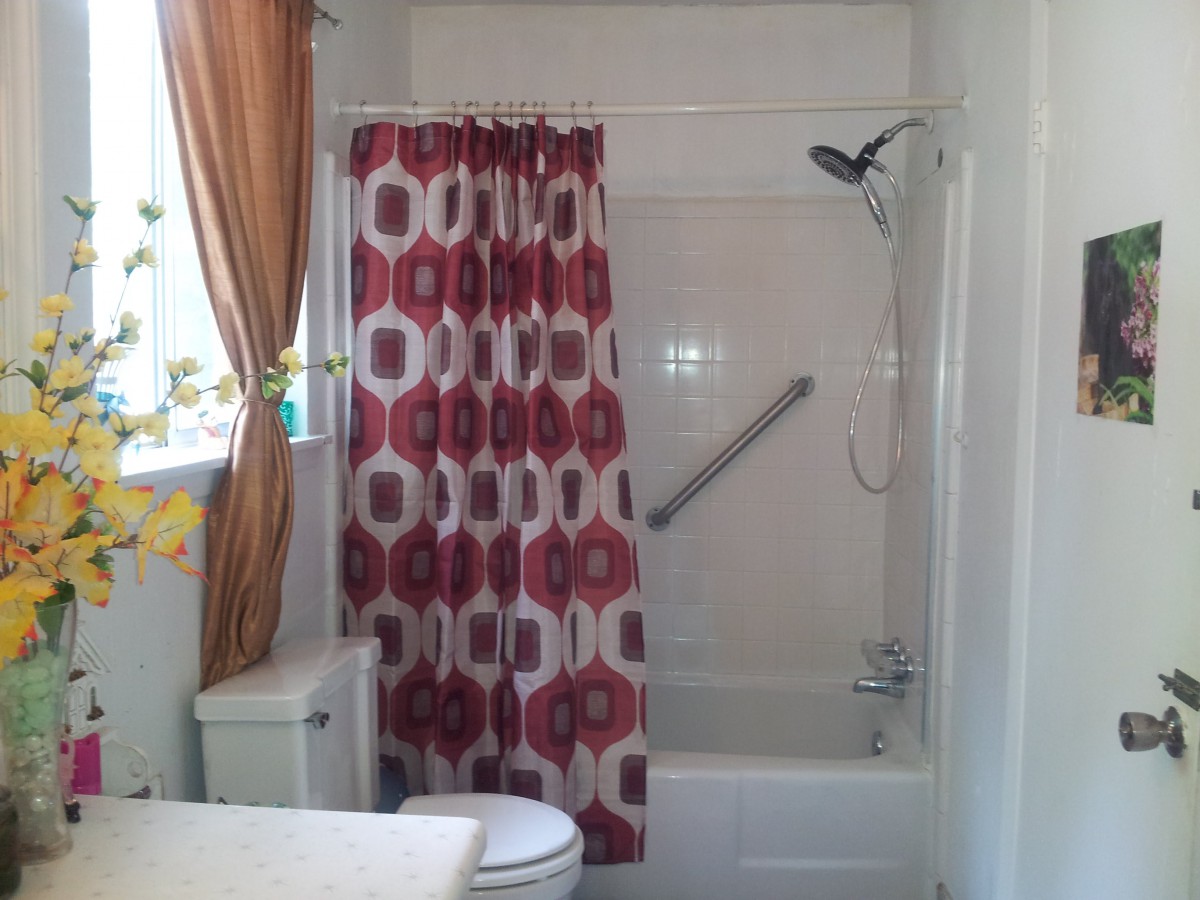 A bathroom interior featuring a bathtub with a red and white patterned shower curtain, a toilet, and curtains over the window.