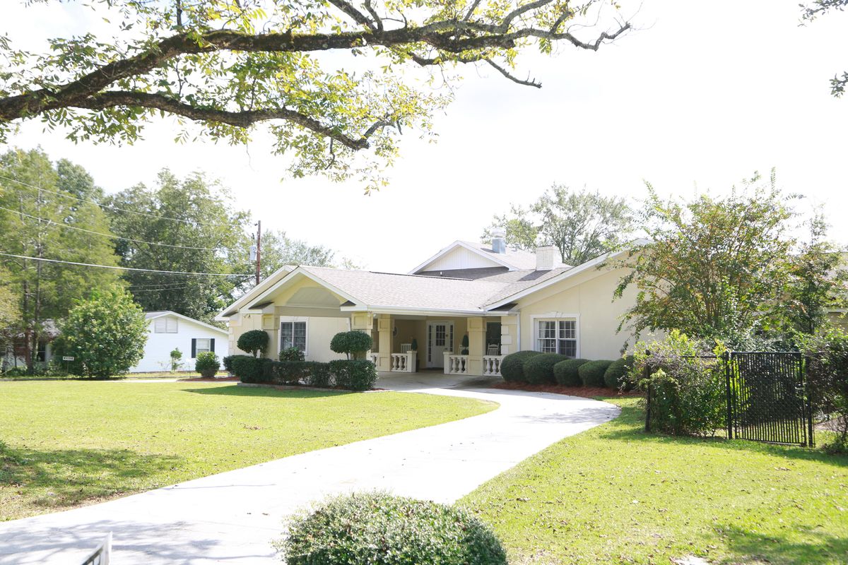A suburban house with a driveway and well-maintained lawn surrounded by trees.