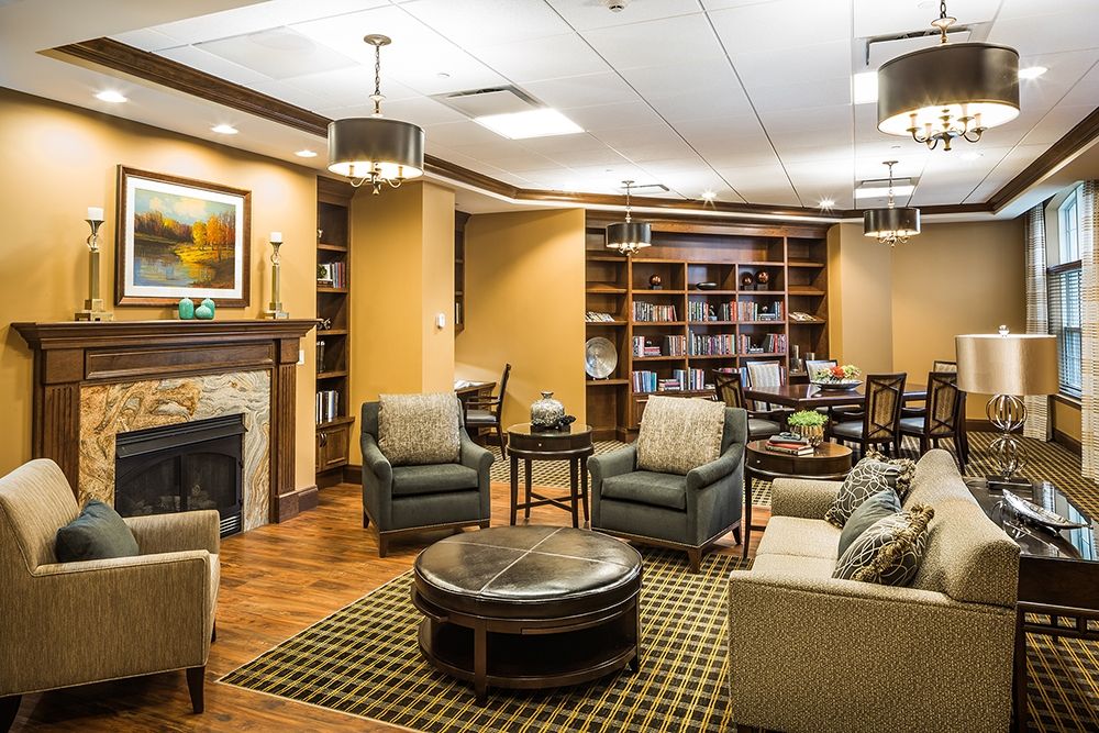 A cozy and well-furnished living room with a library section, featuring comfortable seating, a fireplace, and bookshelves.