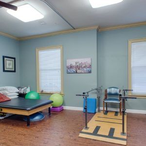 A well-equipped physical therapy room with exercise equipment, including a treatment table, parallel bars, and fitness balls.