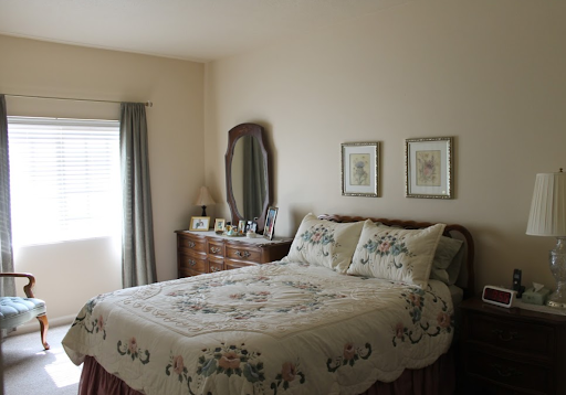 A cozy and neatly arranged bedroom featuring a large quilted bed, elegant mirror, and framed pictures on the wall.
