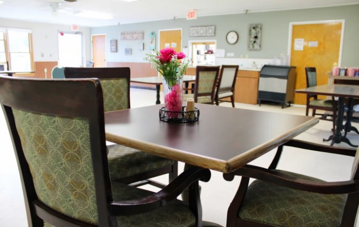 A brightly lit dining area with a table and chairs, featuring a floral centerpiece.