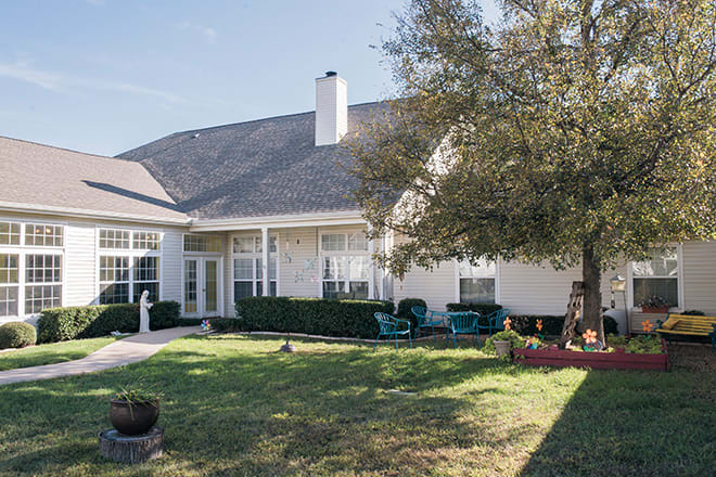 A cozy backyard with patio furniture and a large tree, showcasing a well-maintained lawn in front of a charming house.