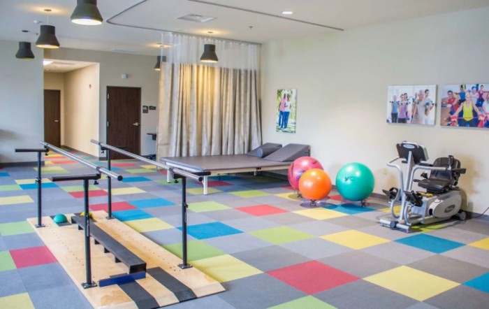 A well-equipped physical therapy room with colorful floor tiles and various exercise equipment, including balance bars and exercise balls.