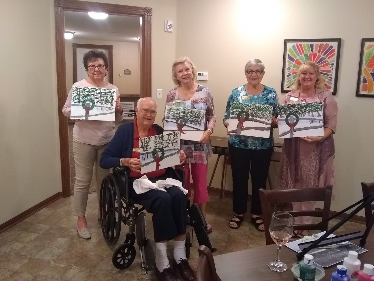 A group of seniors proudly displaying their artwork indoors.