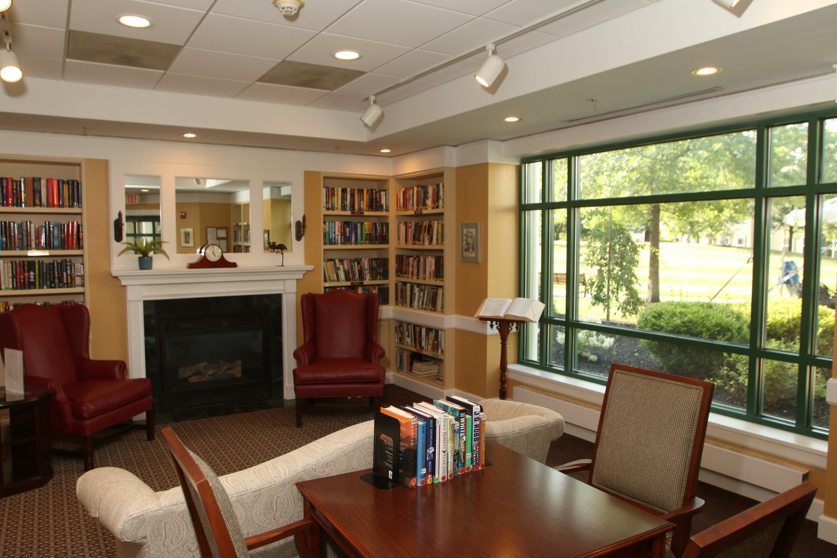 A cozy library reading area with bookshelves, comfortable seating, and a fireplace.