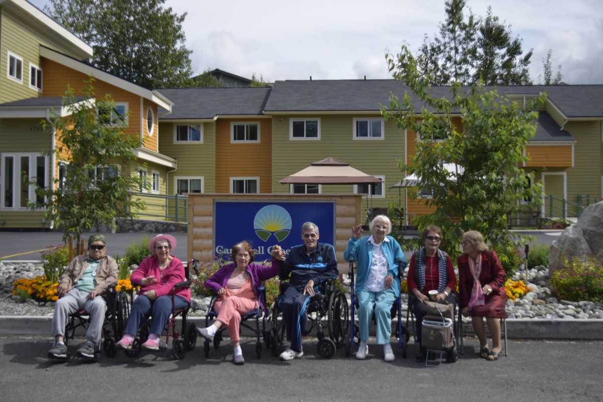 A group of elderly residents sitting outdoors in wheelchairs in front of a nursing home.
