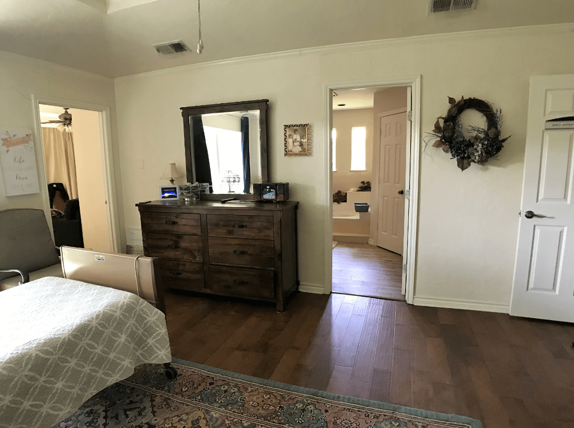 A cozy bedroom with a wooden dresser, mirror, and open doorway leading to another room.