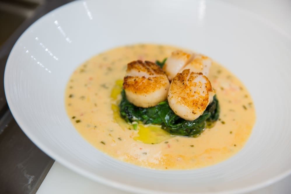 A gourmet dish featuring seared scallops on a bed of spinach with a creamy sauce.