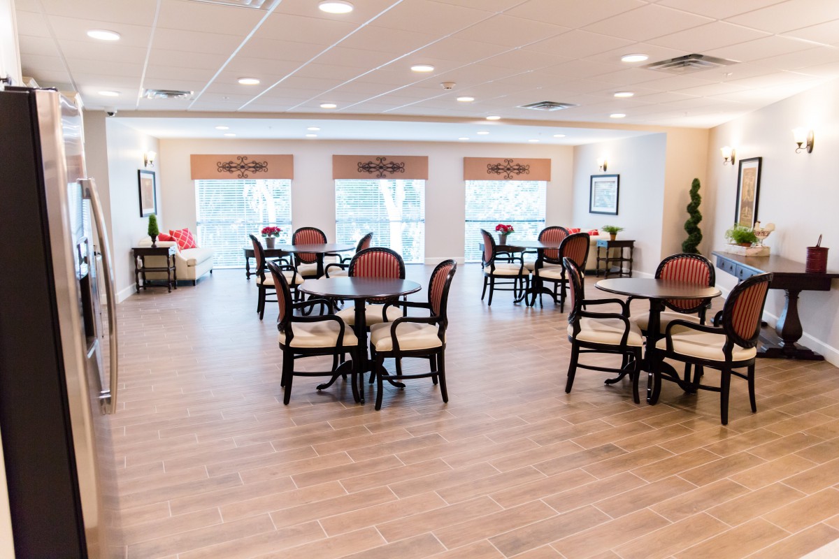 A spacious and elegantly designed dining area with multiple tables and chairs, featuring wooden flooring and large windows.
