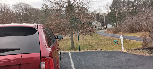 A red vehicle parked beside a grassy area, with trees in the background and a road leading away.