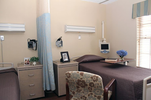 A well-equipped hospital room featuring a bed, bedside furniture, and personal touches.