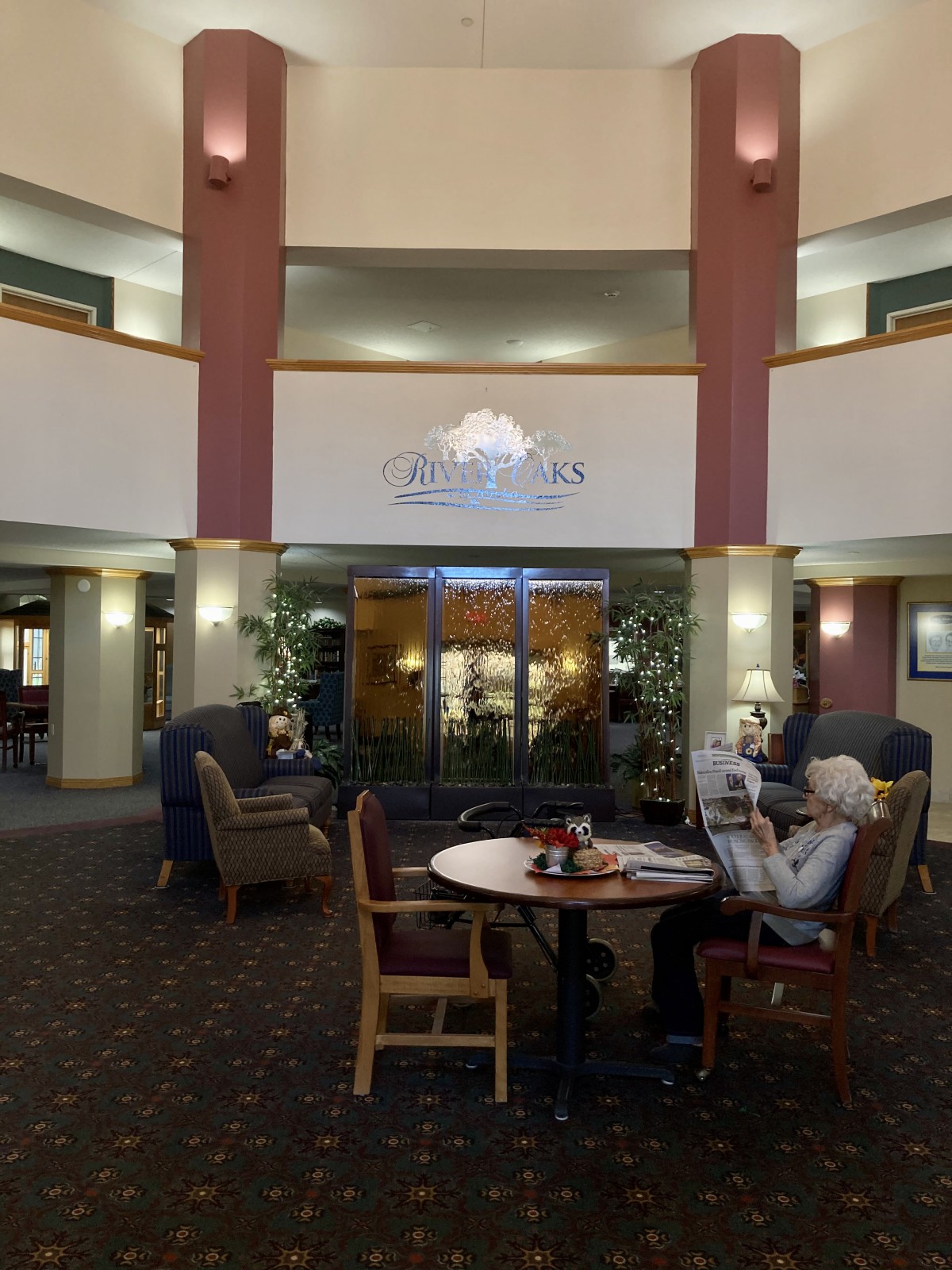 A cozy lobby area with comfortable seating and decorative plants, where elderly individuals enjoy a conversation.