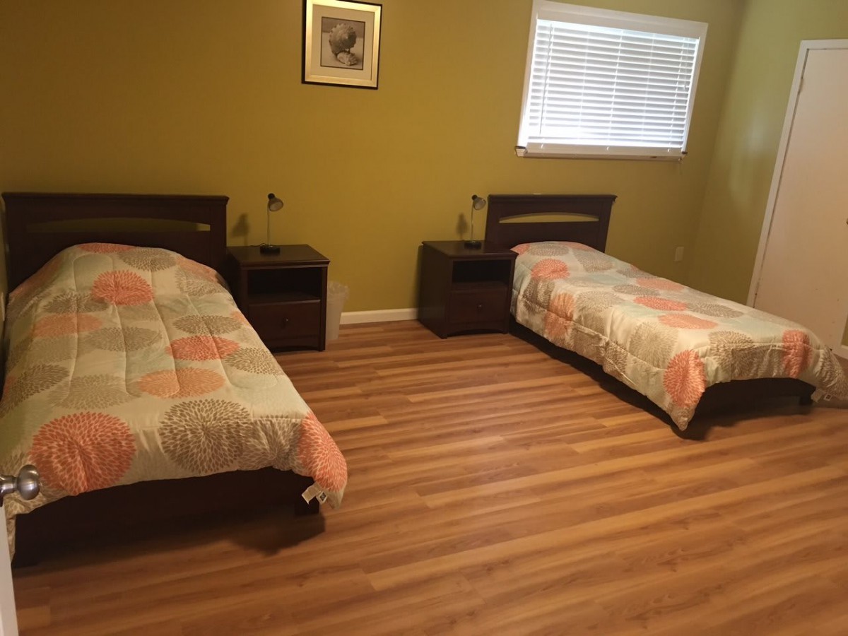 A bedroom with two twin beds, wooden flooring, and a window.