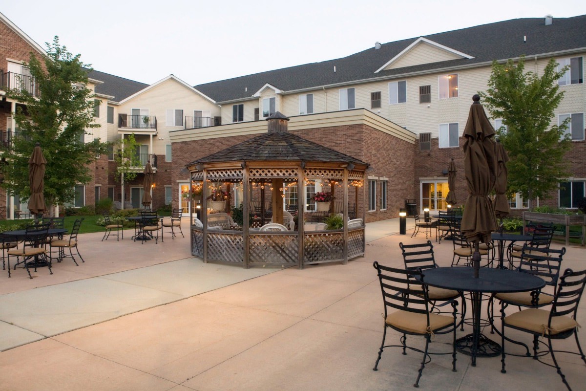 A well-lit gazebo in a courtyard with outdoor seating and surrounding buildings during the evening.